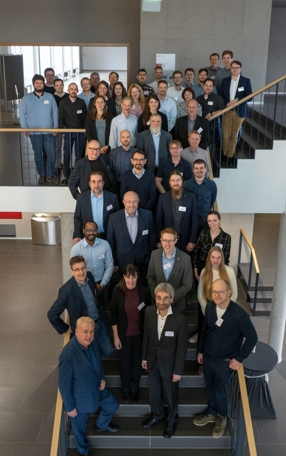 Eine bunt gemischte Gruppe von Männern und Frauen in Business-Kleidung steht für ein Gruppenfoto auf einer Treppe in einem modernen Gebäude. Die Namensschilder weisen auf ihre Fachgebiete hin und scheinen sich für eine Fachveranstaltung zum Thema Medizintechnik versammelt zu haben. at Hochschule Coburg