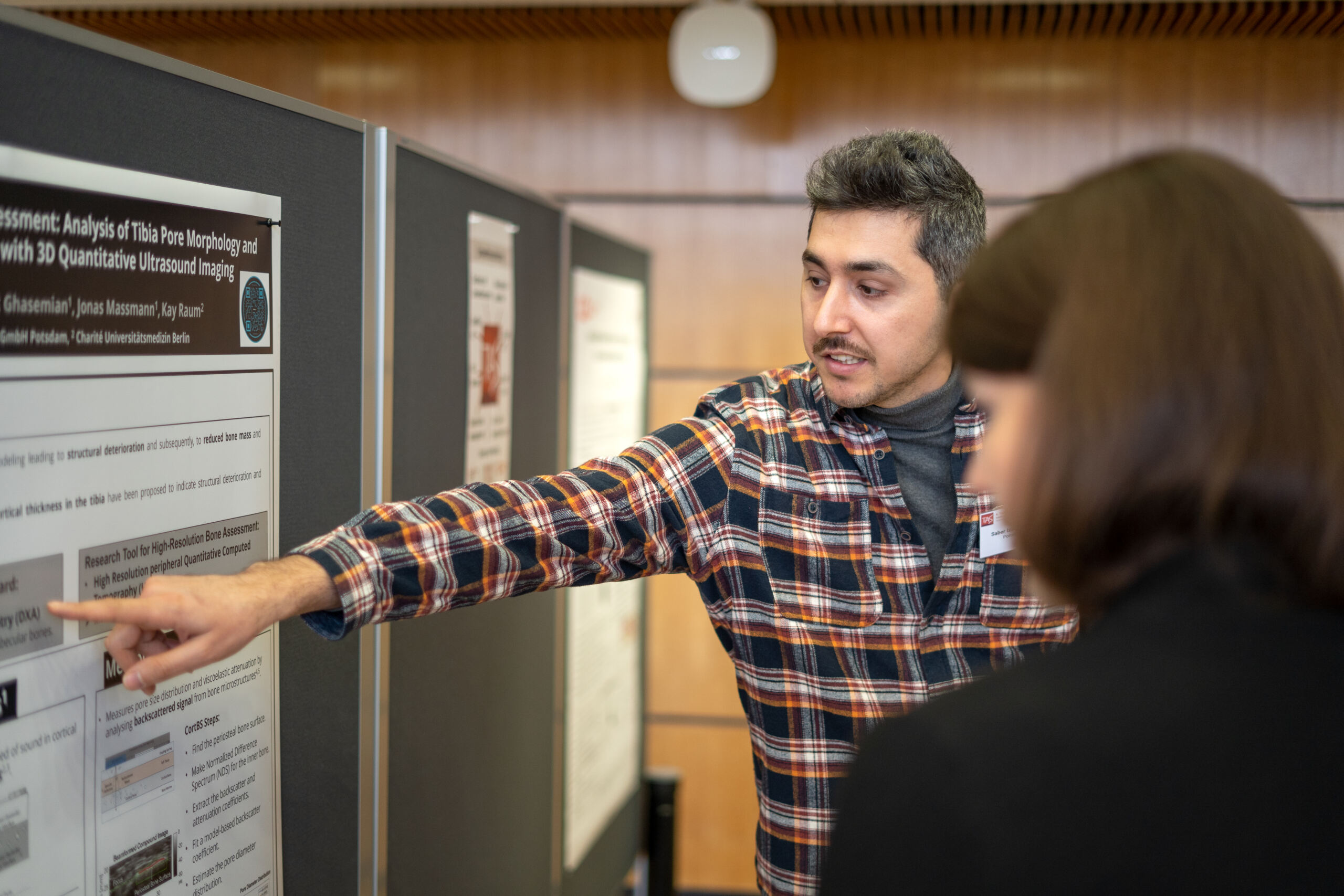 Eine Person im karierten Hemd präsentiert bei einer akademischen Veranstaltung in geschlossenen Räumen ein Poster zum Thema Recycling. Sie zeigt auf einen Abschnitt, während sie einem Teilnehmer etwas erklärt. Der Raum ist mit Holzpaneelen und Pinnwänden ausgestattet, die eine konzentrierte und dennoch einladende Atmosphäre schaffen. at Hochschule Coburg